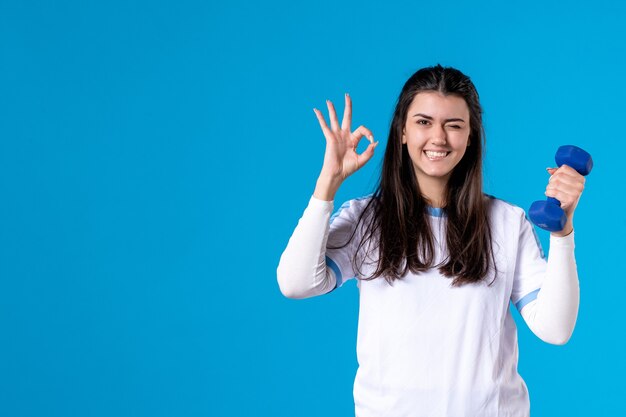 Jovem mulher segurando um haltere azul na parede azul de frente