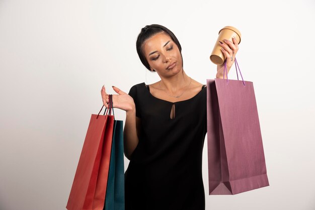 Jovem mulher segurando um monte de sacolas de compras e uma xícara de café.