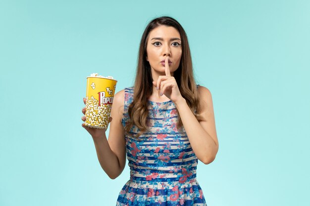 Foto grátis jovem mulher segurando um pacote de pipoca e assistindo filme na superfície azul