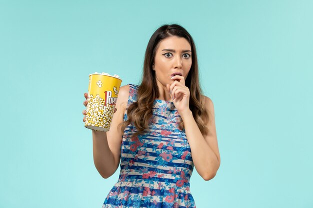 Jovem mulher segurando um pacote de pipoca e assistindo filme na superfície azul