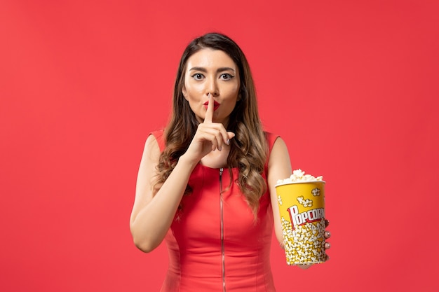 Foto grátis jovem mulher segurando um pacote de pipoca na mesa vermelha clara de frente