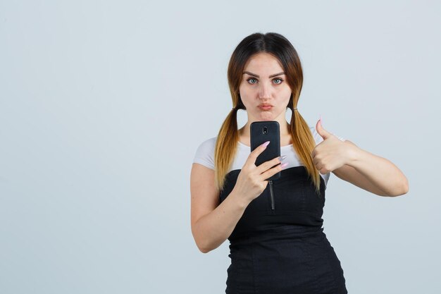 Jovem mulher segurando um smartphone enquanto mostra o polegar para cima