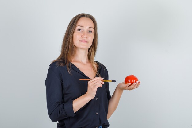 Jovem mulher segurando um tomate falso com pincel na camisa preta
