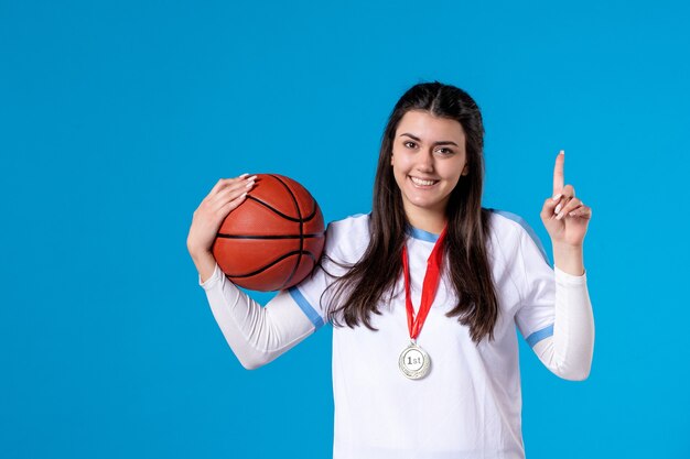 Jovem mulher segurando uma bola de basquete na parede azul de frente