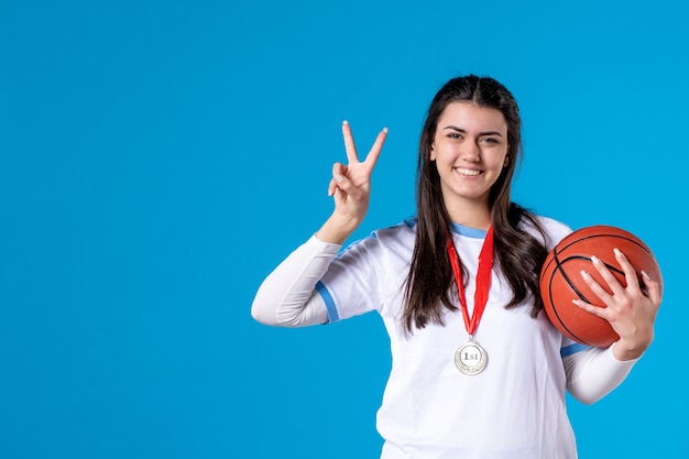 Jovem mulher segurando uma bola de basquete na parede azul de frente