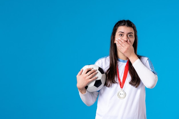 Jovem mulher segurando uma bola de futebol na parede azul de frente