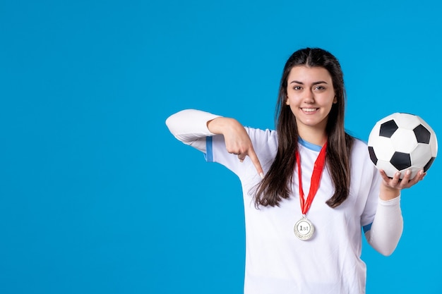 Jovem mulher segurando uma bola de futebol na parede azul de frente