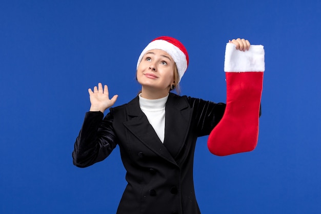 Jovem mulher segurando uma meia vermelha de natal na parede azul humana, de frente para o ano novo.