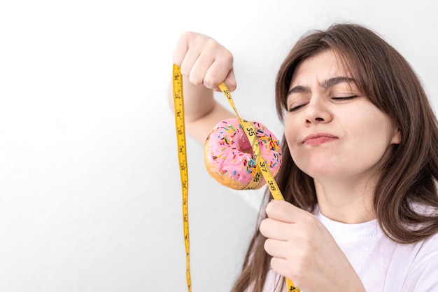 Jovem mulher segurando uma rosquinha com fita métrica isolada