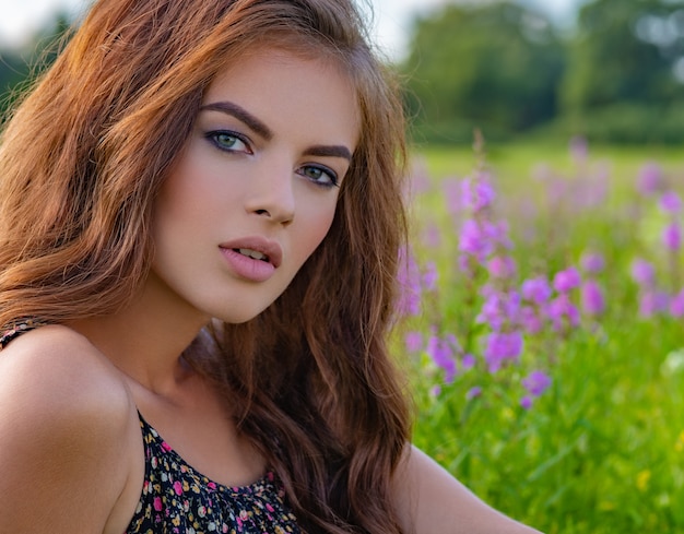 Jovem mulher sentada ao ar livre em um campo de flores roxas. modelo posando em flores de lavanda.