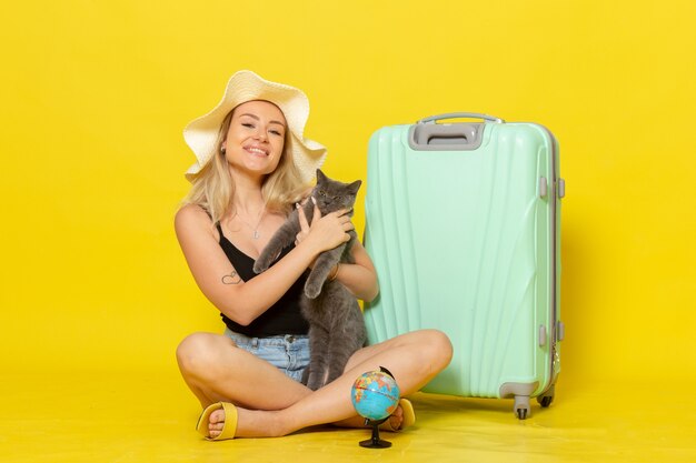 Jovem mulher sentada com sua bolsa verde segurando o gatinho na parede amarela viagem de férias viagem marítima sol
