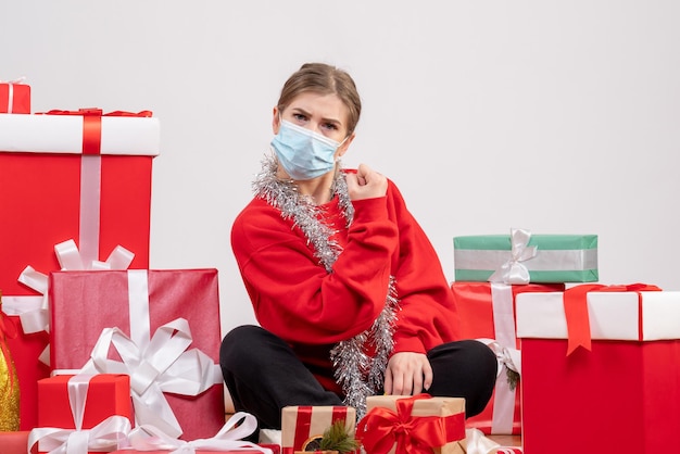 Jovem mulher sentada de frente com os presentes de Natal em máscara estéril