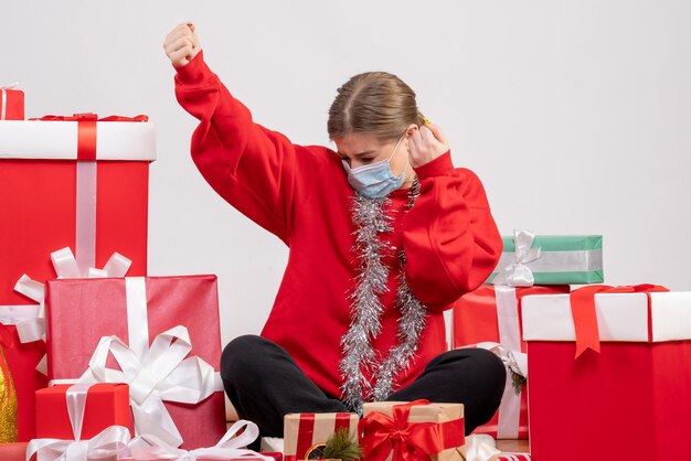 Jovem mulher sentada de frente com os presentes de Natal na máscara