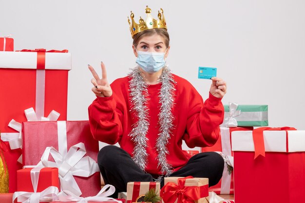 Jovem mulher sentada de frente com os presentes de natal segurando um cartão do banco