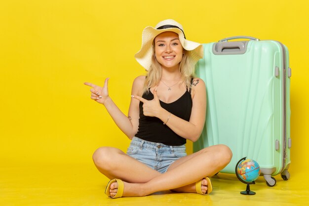 Jovem mulher sentada de frente com sua bolsa e se sentindo feliz no sol parede amarela viagem férias viagem mar jornada