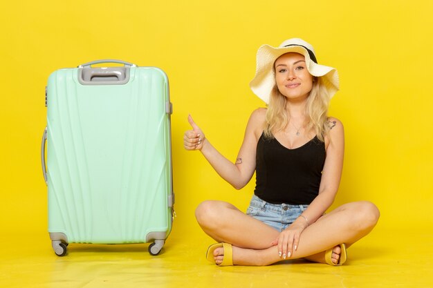 Jovem mulher sentada de frente com sua bolsa verde na parede amarela viagem férias sol viagem viagem garota