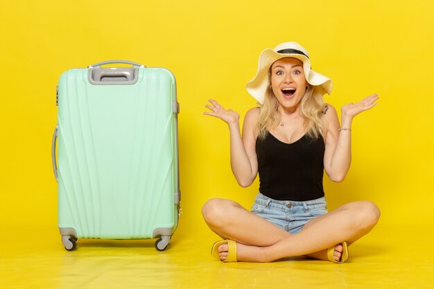 Jovem mulher sentada de frente com sua bolsa verde se sentindo feliz na parede amarela viagem férias viagem jornada garota