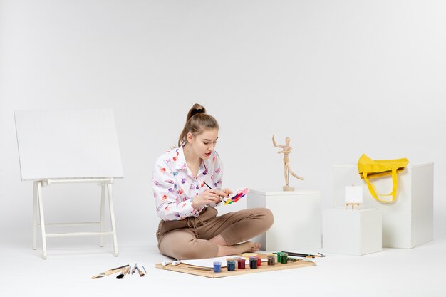 Jovem mulher sentada de frente com tintas e cavalete para desenhar em fundo branco
