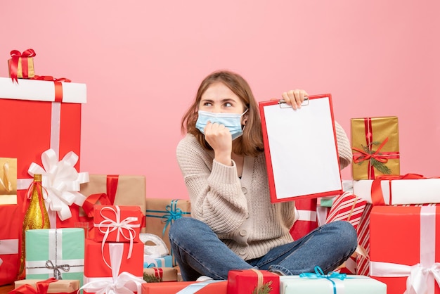 Jovem mulher sentada de frente para o natal presentes na máscara com um bilhete