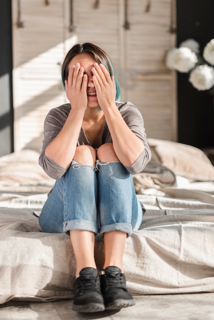 Jovem mulher sentada na cama, fechando os olhos