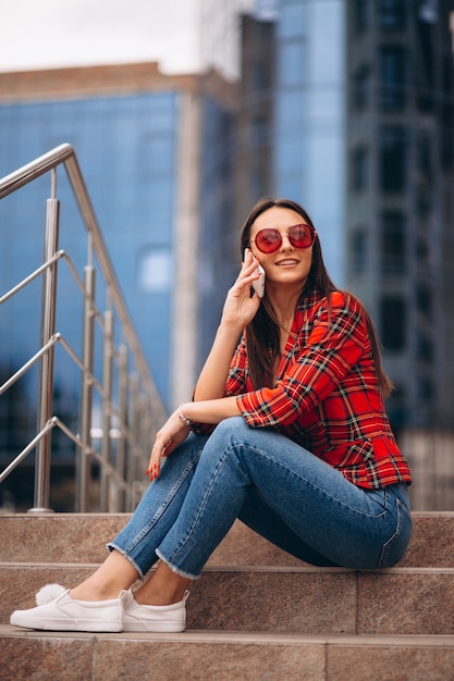 Jovem mulher sentada na escada e falando ao telefone