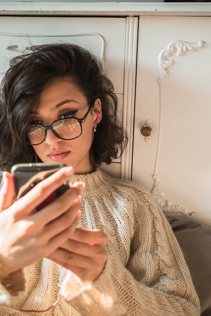 Jovem mulher sentada perto de guarda-roupa e usando smartphone