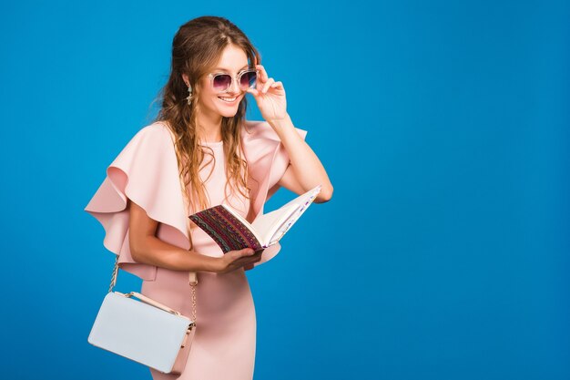 Jovem mulher sexy elegante em um vestido de luxo rosa, tendência da moda para o verão, estilo chique, óculos de sol, fundo de estúdio azul, bloger de moda