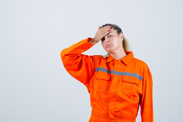 Jovem mulher sofrendo de dor de cabeça com uniforme de trabalhador e parecendo desconfortável. vista frontal.