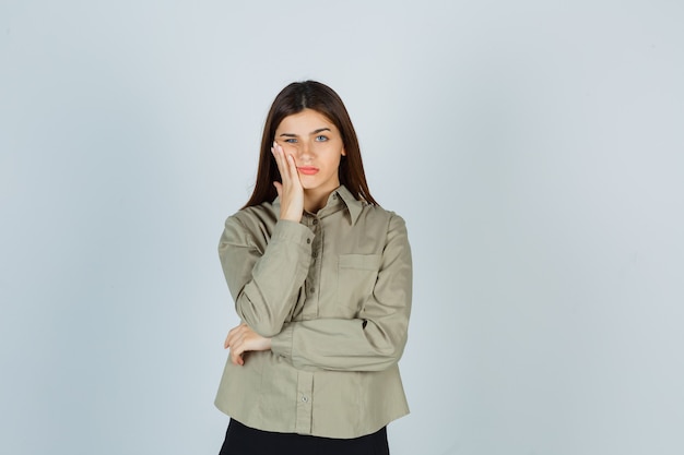 Jovem mulher sofrendo de dor de dente na camisa, saia e parecendo dolorosa, vista frontal.