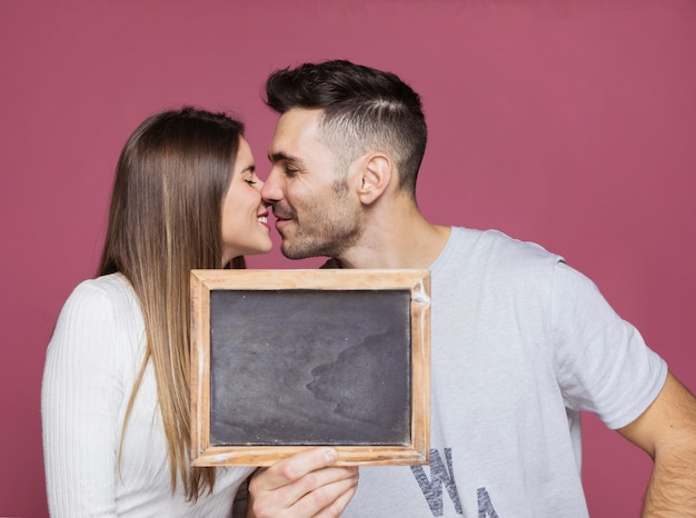 Jovem mulher sorridente beijando com homem positivo e mostrando o frame da foto