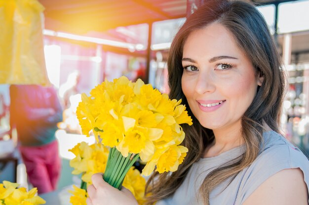 Jovem, mulher sorridente selecionando flores frescas. Feche o retrato do perfil de uma bela e jovem curtindo um buquê de flores enquanto estiver em uma barraca de mercado floral fresca durante um dia ensolarado ao ar livre.