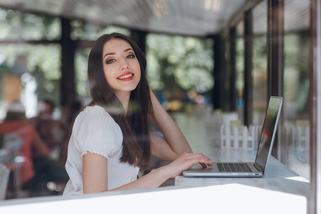 Jovem, mulher, sorrindo, enquanto escrevendo em seu laptop