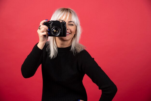 Jovem mulher tirando fotos com uma câmera sobre um fundo vermelho. Foto de alta qualidade