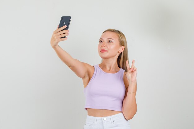 Jovem mulher tirando uma selfie mostrando o sinal V na camiseta