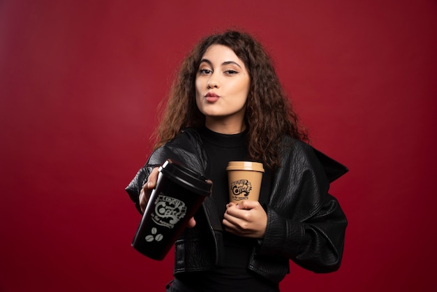 Jovem mulher toda vestida de preto, mostrando duas xícaras.