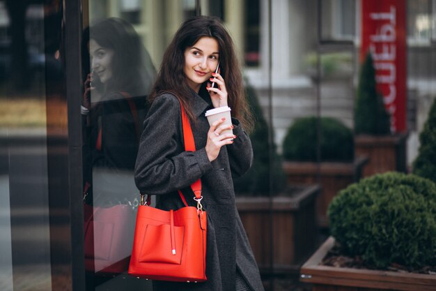 Jovem mulher tomando café e usando o telefone na cidade