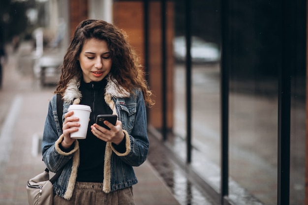 Jovem mulher tomando café e usando o telefone