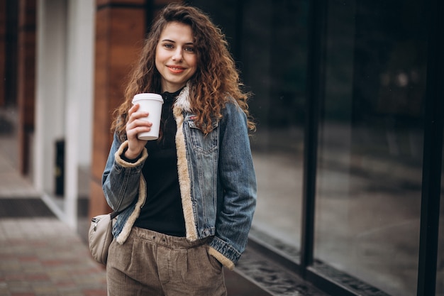 Jovem mulher tomando café e usando o telefone