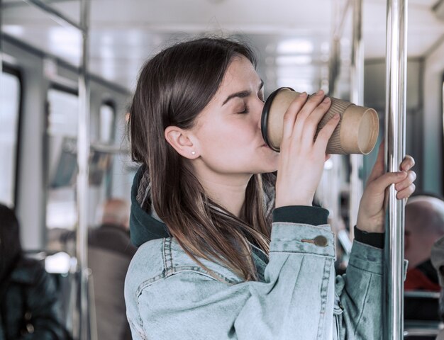 Jovem mulher tomando café no transporte público.