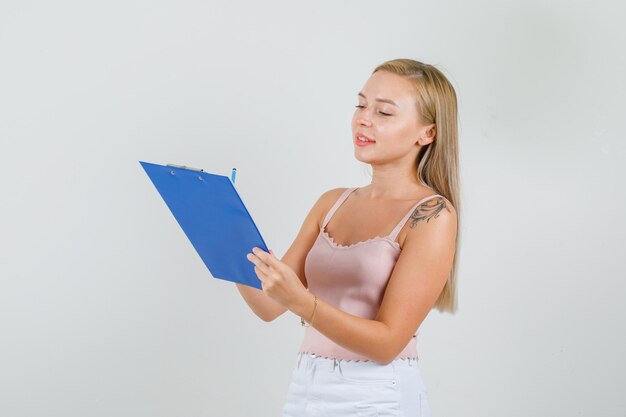 Jovem mulher tomando notas na área de transferência em camiseta, minissaia e parecendo ocupada.