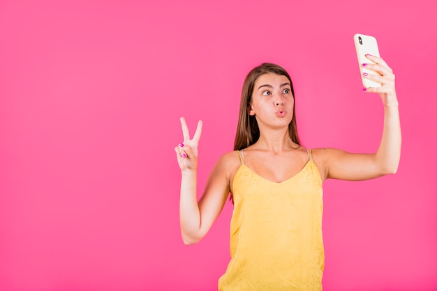 Jovem mulher tomando selfie em fundo rosa