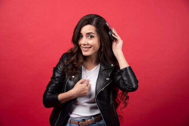 Jovem mulher usando fones de ouvido e posando em um fundo vermelho. Foto de alta qualidade