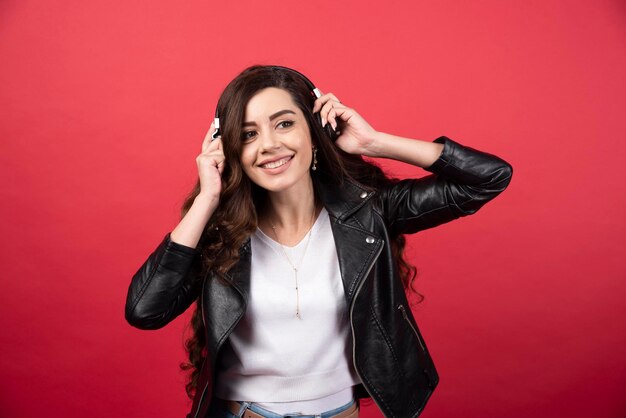 Jovem mulher usando fones de ouvido e posando em um fundo vermelho. Foto de alta qualidade