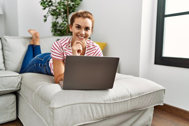 Jovem mulher usando laptop deitado no sofá em casa