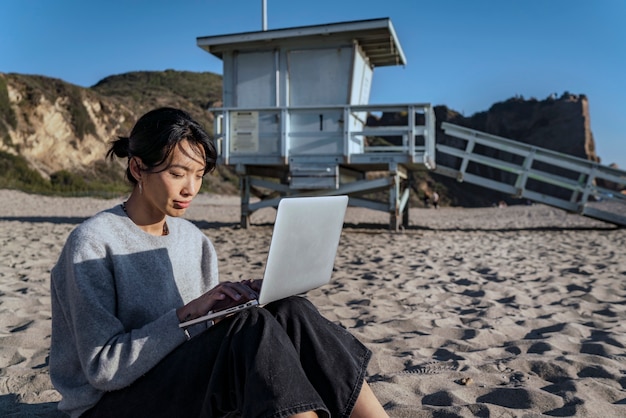 Foto grátis jovem mulher usando seu laptop na praia