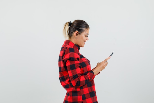 Jovem mulher usando telefone celular com camisa e parece alegre.