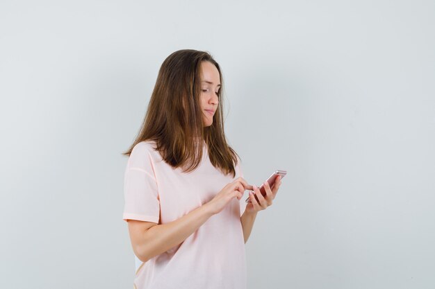 Jovem mulher usando telefone celular em t-shirt rosa e olhando ocupada, vista frontal.