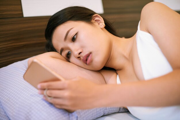 Jovem mulher usando telefone enquanto estava deitado na cama