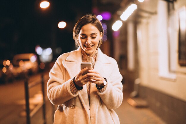 Jovem mulher usando telefone fora da rua à noite