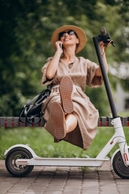 Jovem mulher usando telefone no parque, sentado no banco pela scooter